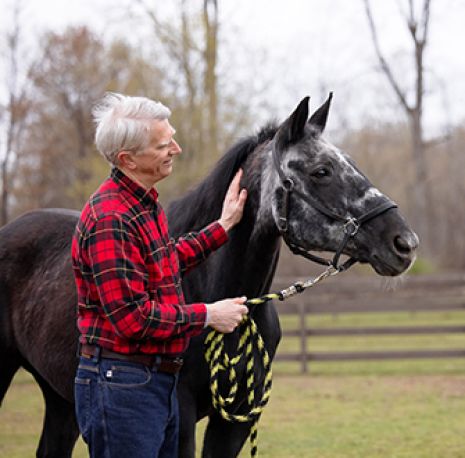an older man wearing red plaid walking next to a horse